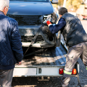 Tow truck driver securing a wrecked vehicle onto a towing trailer